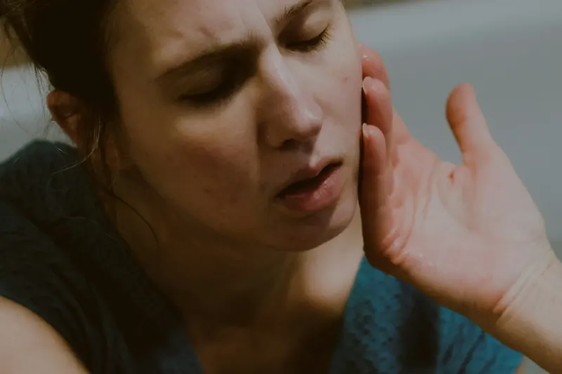 Una mujer con la mano en la cara y gesto de dolor