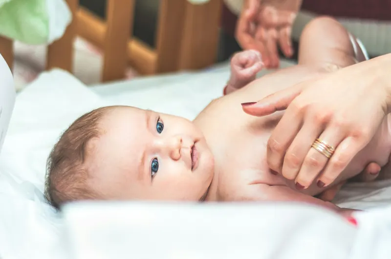 Las manos de una adulta sobre la tripa de un bebé tumbado